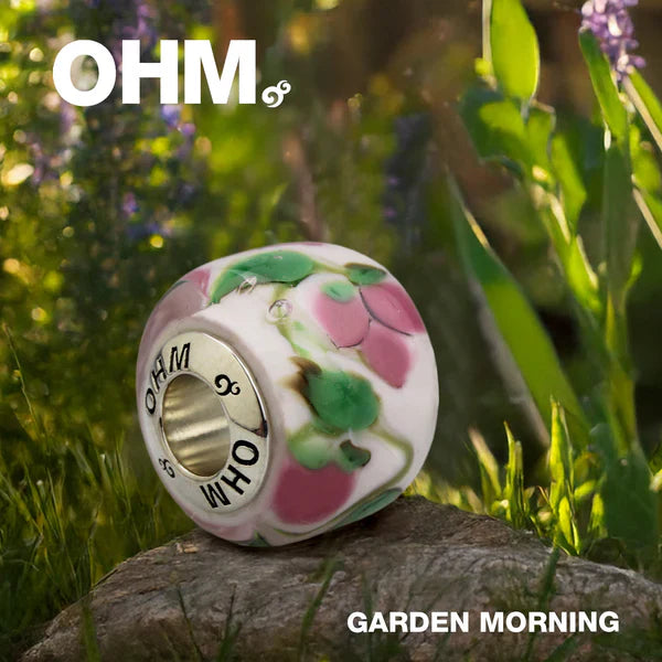 Decorative bead with floral design on a stone in a garden setting, featuring the brand 'OHM'.